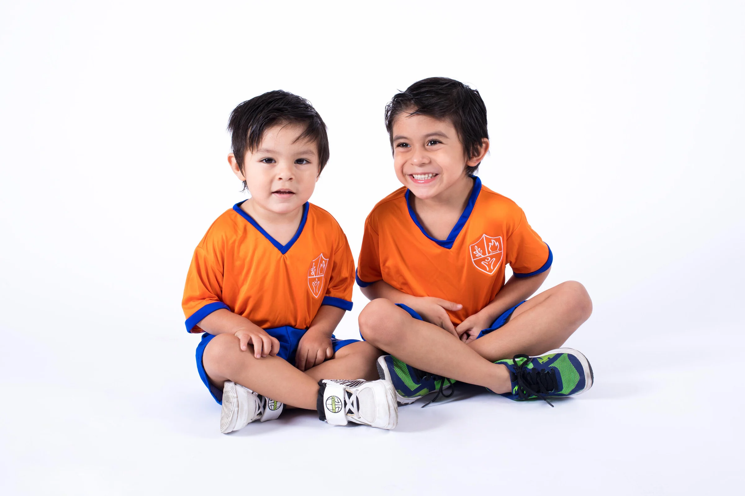 Two Instituto San Gerardo boys sitting and smiling in orange uniforms