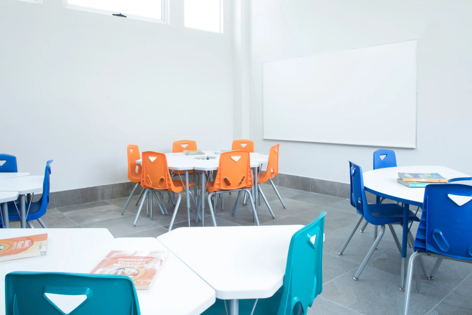 Bright classroom with tables, orange and blue chairs and a whiteboard