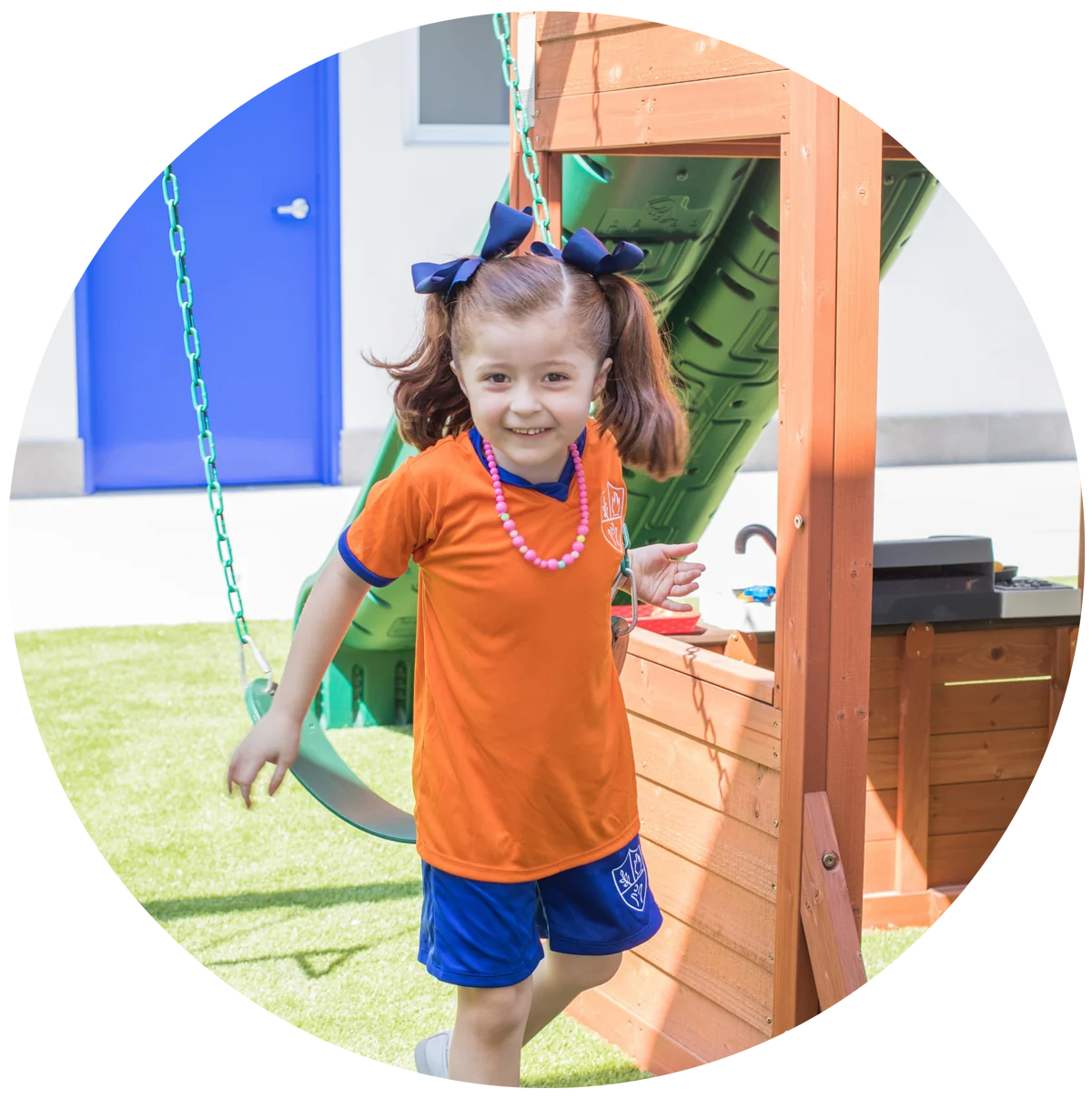 Smiling girl next to a wooden play structure with a swing and a slide in the yard