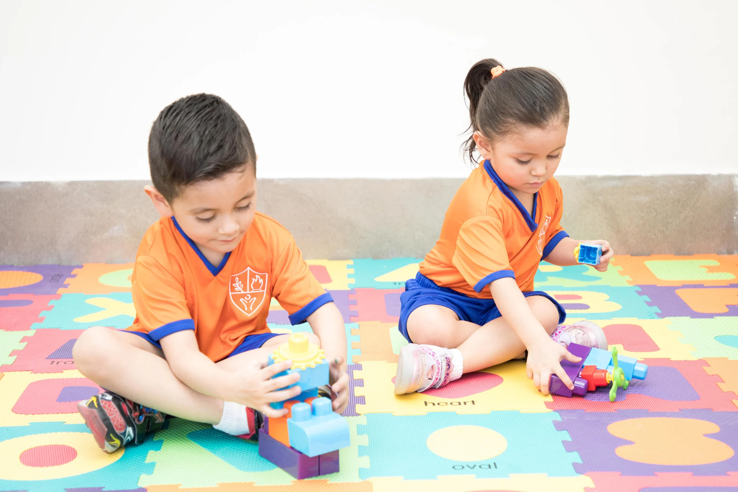 Two Instituto San Gerardo children playing with blocks on a colorful mat