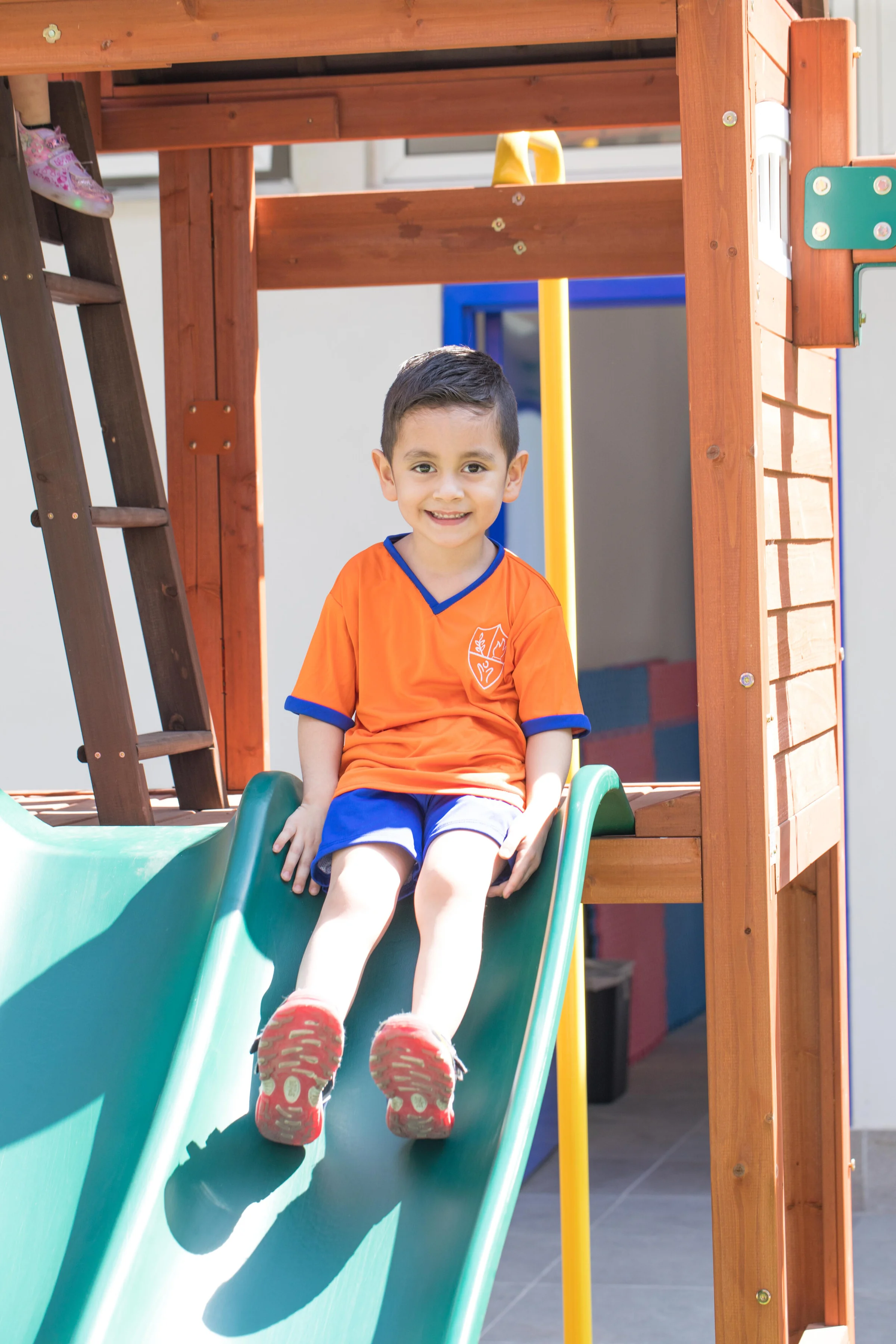 Smiling boy in the Instituto San Gerardo uniform next to a wooden playground structure