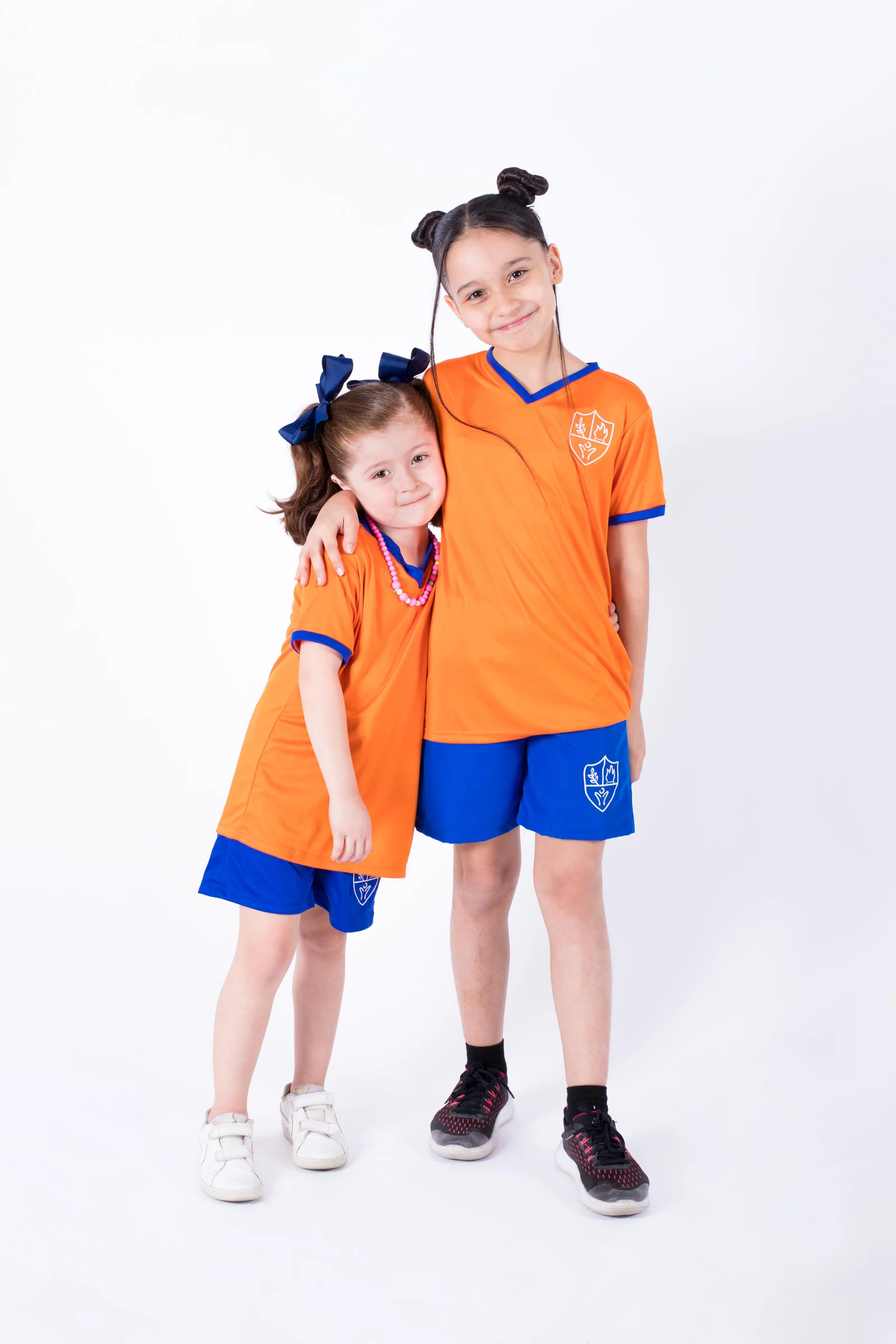 Two Instituto San Gerardo girls in orange uniforms, hugging