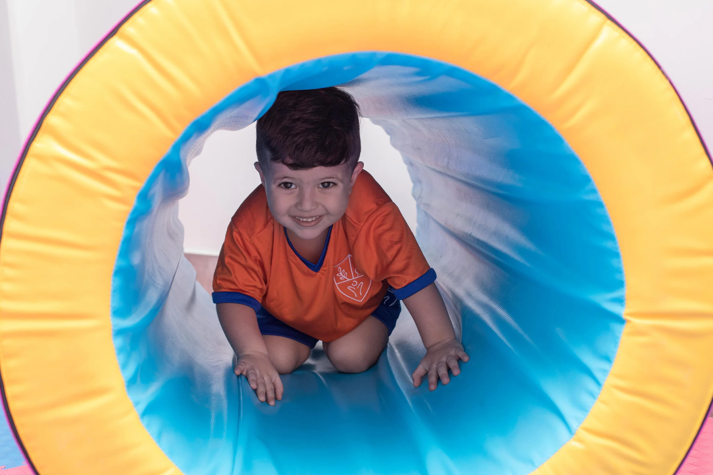 Smiling Instituto San Gerardo boy crawling through a play tunnel